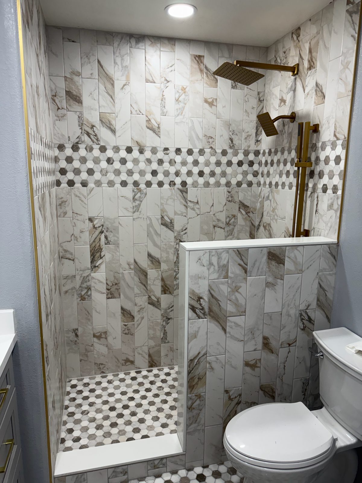 Marble-look walk-in shower with a hexagon mosaic band and gold rain shower head